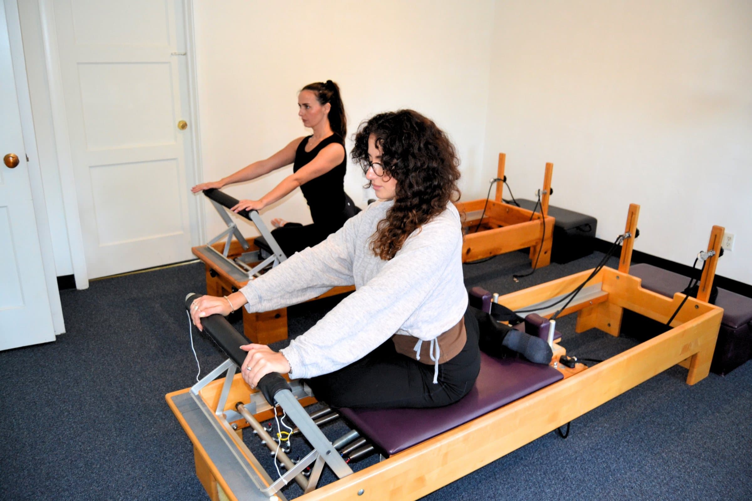 Two clients on reformers pressing the footbar, side by side, during a small group class at Embodied Pilates