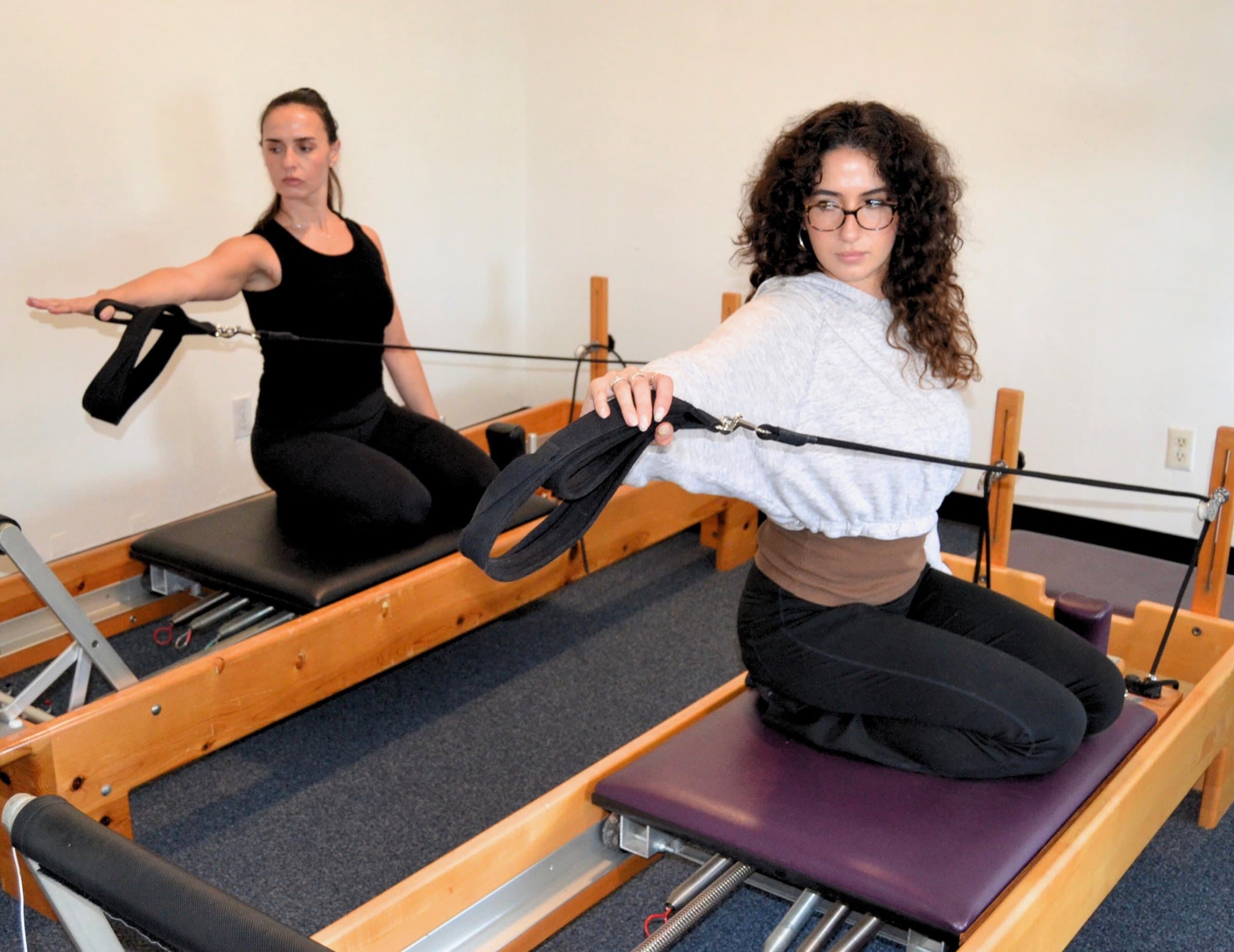 Two clients kneeling on reformers, arms extended with the straps, at Embodied Pilates