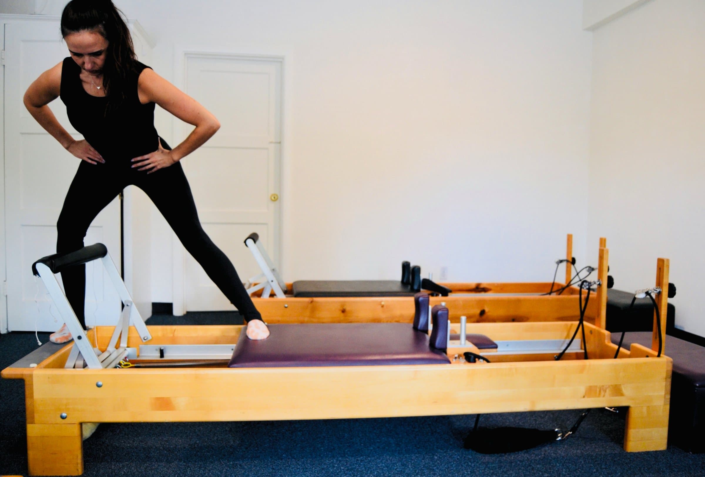 A client standing on a reformer in a lunge, hands on hips, during a private session at Embodied Pilates